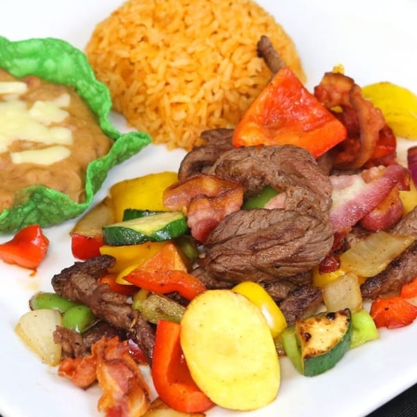 Grilled steak, bacon, and colorful vegetables with a side of rice and refried beans.