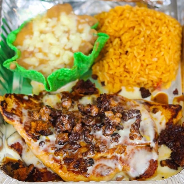 Chicken dish topped with cheese and chorizo, served with yellow rice and refried beans in a green tortilla cup.