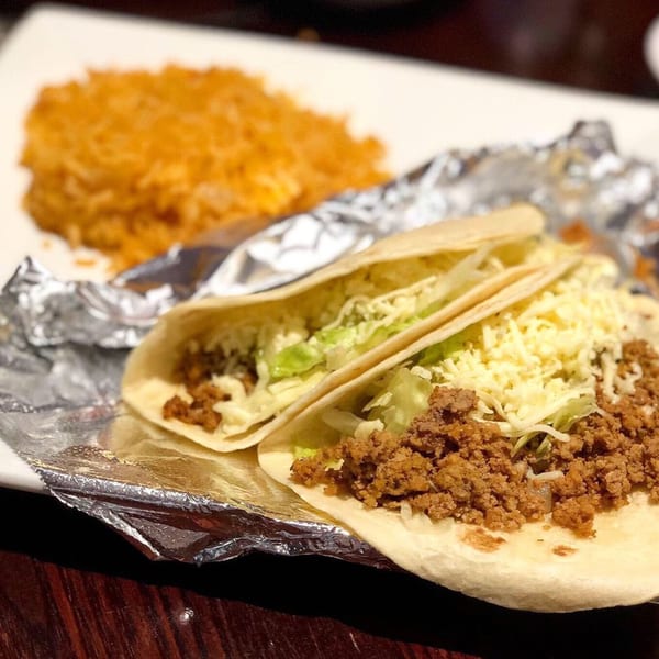 Two soft tacos with ground beef, shredded lettuce, and cheese, served with rice on a white plate.