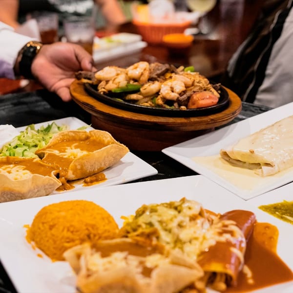 A hand serving a sizzling platter of shrimp and steak fajitas with other Mexican dishes.