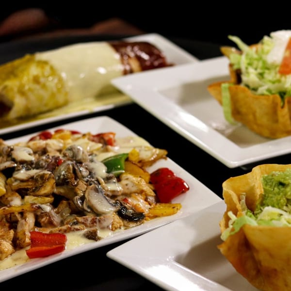 Assortment of Mexican dishes including fajitas, burritos, and taco salads on white plates.